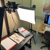 A specimen being imaged in the digitisation suite. It sits on a copy stand with two flash heads at either side and a camera suspended above. A computer is on in the background.