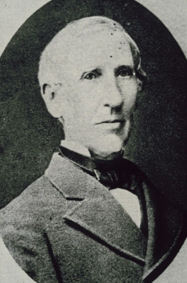 A black and white portrait photo of Sonder. He is wearing a grey suit jacket over a black cravat and white shirt. 
